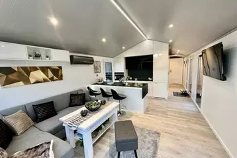 Modernes offenes Wohnzimmer und Küche mit eleganten Möbeln, einem Sofa, Barhockern und zeitgenössischem Dekor.