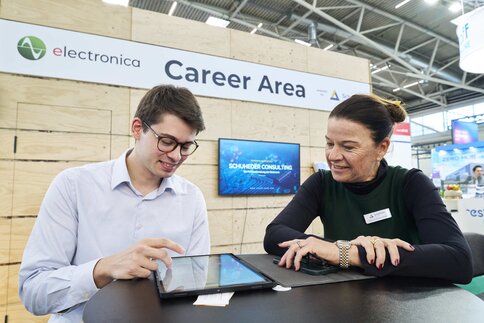 Zwei Personen sitzen in einem Karrierebereich an einem Tisch und besprechen etwas auf einem Tablet.
