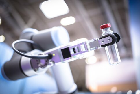 Ein Roboterarm hält ein Reagenzglas an einem Messestand