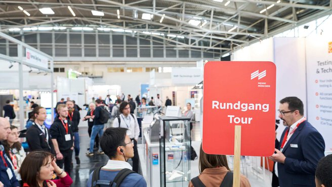 Guided trade fair tour with a group of visitors and a “Tour” sign.