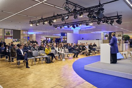Fachvortrag auf Messebühne mit Rednerin am Pult und Publikum in modern beleuchtetem Konferenzbereich.
