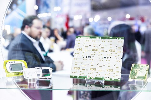 Close-up of electronic components and circuit boards on display in a glass cabinet. People can be seen out of focus in the background.