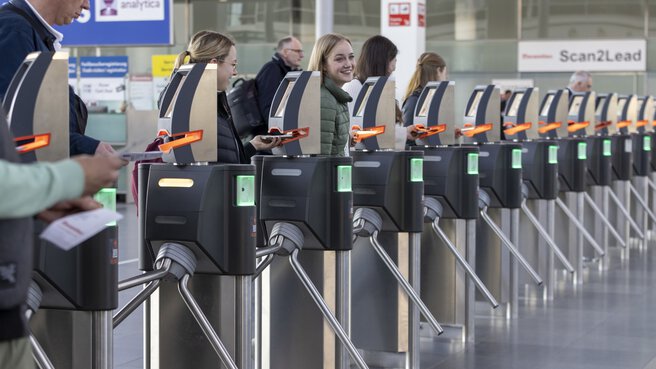 Lächelnde Menschen gehen durch die automatischen Ticketschranken am Messe Eingang.