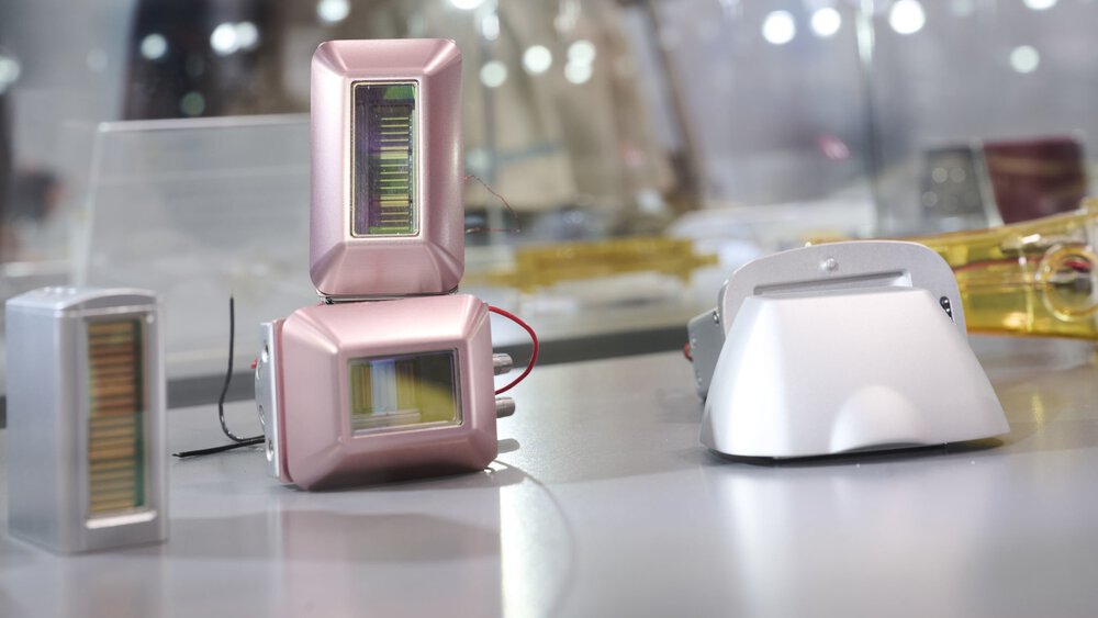 Several compact optoelectronic sensor modules with rectangular housings and visible color filters are displayed on an exhibition surface.
