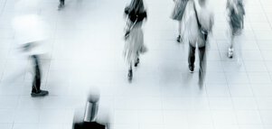 Verschwommene Aufnahme von oben von Menschen, die auf einem gefliesten Boden gehen, die ein Gefühl von Bewegung und Geschäftigkeit vermittelt.