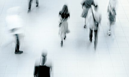 Verschwommene Aufnahme von oben von Menschen, die auf einem gefliesten Boden gehen, die ein Gefühl von Bewegung und Geschäftigkeit vermittelt.