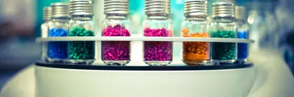 Nahaufnahme eines Analysegeräts: In runden Halterungen sind im Kreis mehrere Fläschchen mit Aluminium-Septumverschluss (Vials) mit bunten Körnern gefüllt angeordnet.