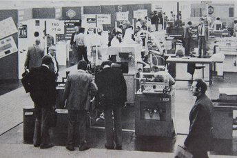Schwarz-weiß Aufnahme der productronica Messe 1975 mit Besuchern an verschiedenen Maschinen- und Technologieständen.