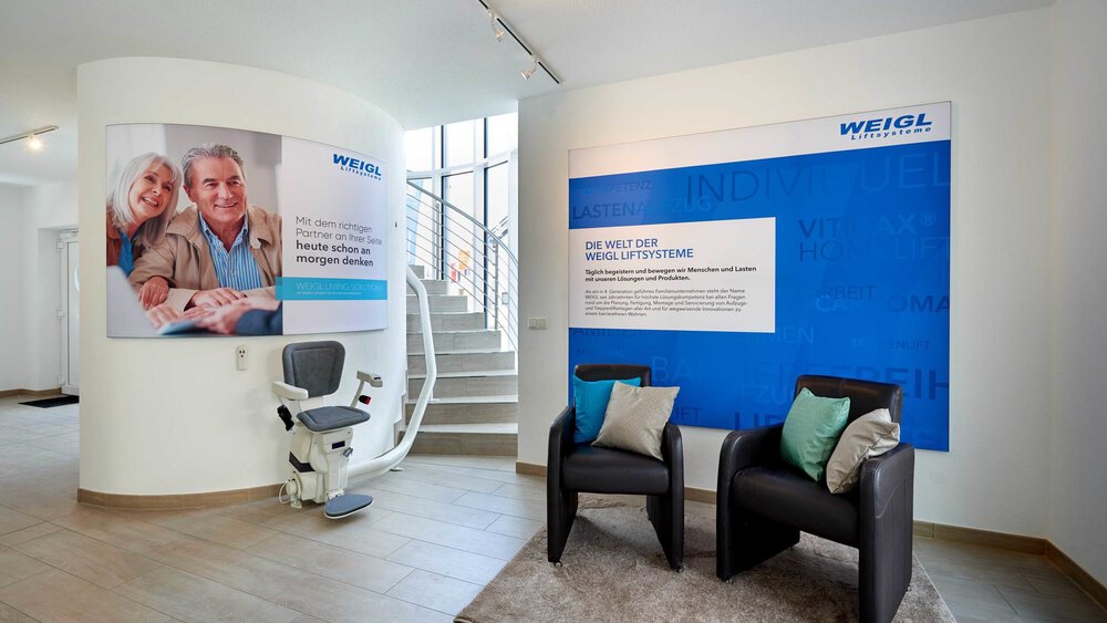 Moderner Raum mit Informationstafeln, Treppenlift, zwei schwarzen Stühlen und dekorativen Kissen.