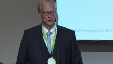 Ein Mann im Anzug spricht an einem Rednerpult vor einer Präsentationsleinwand.