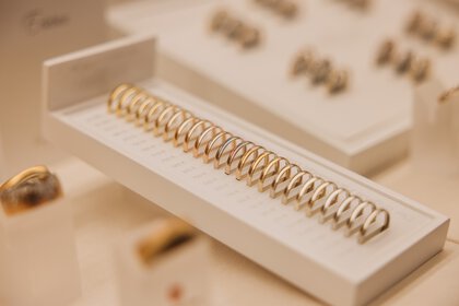 Numerous gold rings are arranged on a white display, sorted by size.