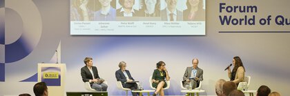 Podiumsdiskussion zum Thema „Quantum Technologies in a Changing World: Geopolitical Impacts and Opportunities“, fünf Personen sitzen auf der Bühne, davor Publikum in einer Messeumgebung.