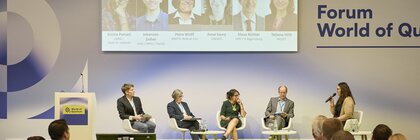 Podiumsdiskussion zum Thema „Quantum Technologies in a Changing World: Geopolitical Impacts and Opportunities“, fünf Personen sitzen auf der Bühne, davor Publikum in einer Messeumgebung.