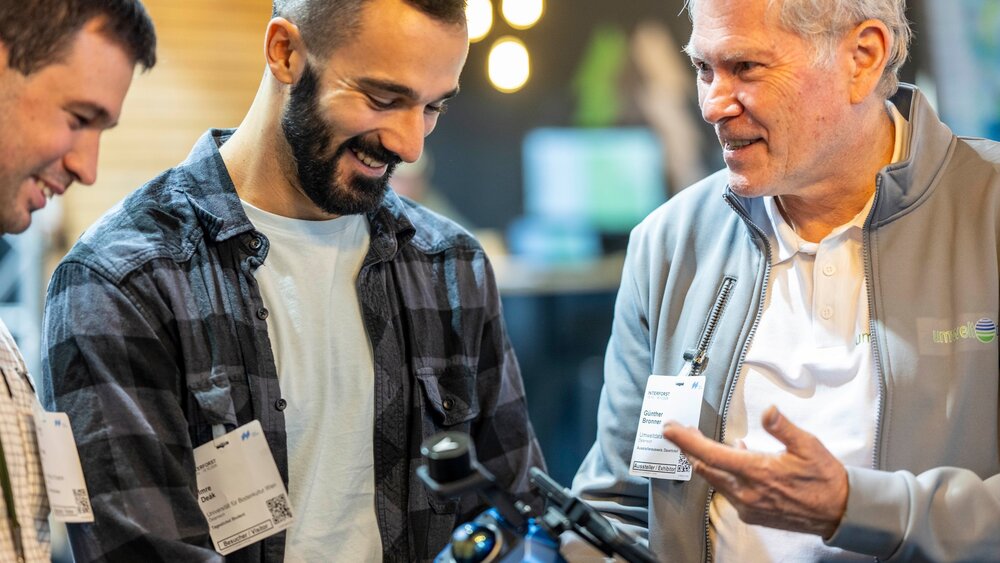 Three men looking at a technical device together at an exhibition stand.