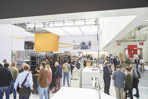 Menschen stehen zwischen ausgestellten Maschinen auf der productronica und lassen sich von den Ausstellern informieren.