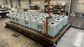 Große Container auf einer Plattform in einem Industrielager mit Regalen und Geräten im Hintergrund.