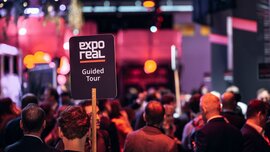EXPO REAL 2026 in Munich: Numerous visitors and a guided tour, marked by an “EXPO REAL Guided Tour” sign, amid a lively trade fair atmosphere.