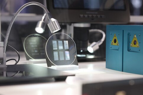 Close-up of a laboratory setup for optical communication technology: round glass plates with fine structures can be seen under selective lighting.
