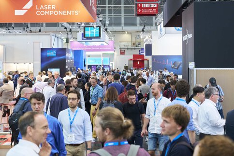A busy exhibition hall with bustling people and stands displaying technical components.
