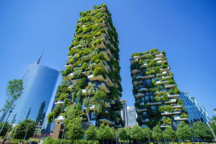 Two tall buildings with lush green balconies and plants against a clear blue sky.