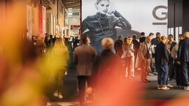Zahlreiche Besucher der INHORGENTA Messe stehen und gehen durch einen Ausstellungsraum, in dem ein großes schwarz-weißes Werbeplakat mit einer Frau steht.