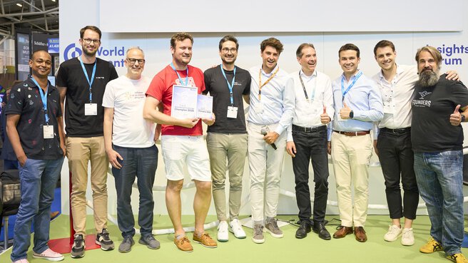 Eine Gruppe von Männern posiert mit Urkunden bei einer Siegerehrung auf der World of Quantum 2025 in München und zeigt Daumen hoch.