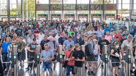  Eine große Menschenmenge wird durch Drehkreuze in einer Halle oder einem Kongresszentrum eingelassen.