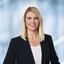 Eine lächelnde Frau mit langen blonden Haaren in einem dunklen Blazer und einem weißen Oberteil.