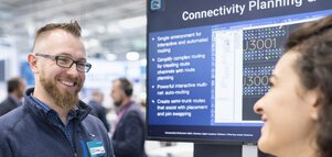 Conversation between exhibitor and attendee at a DMEA booth with digital solutions displayed on a screen