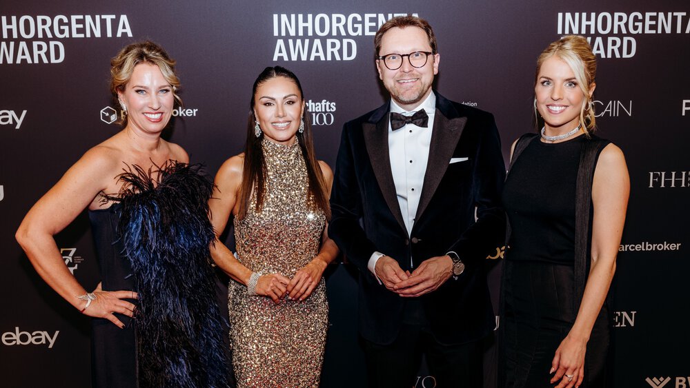A man and three women in festive attire stand smiling in front of a photo wall of the INHORGENTA AWARD and pose for a photo.
