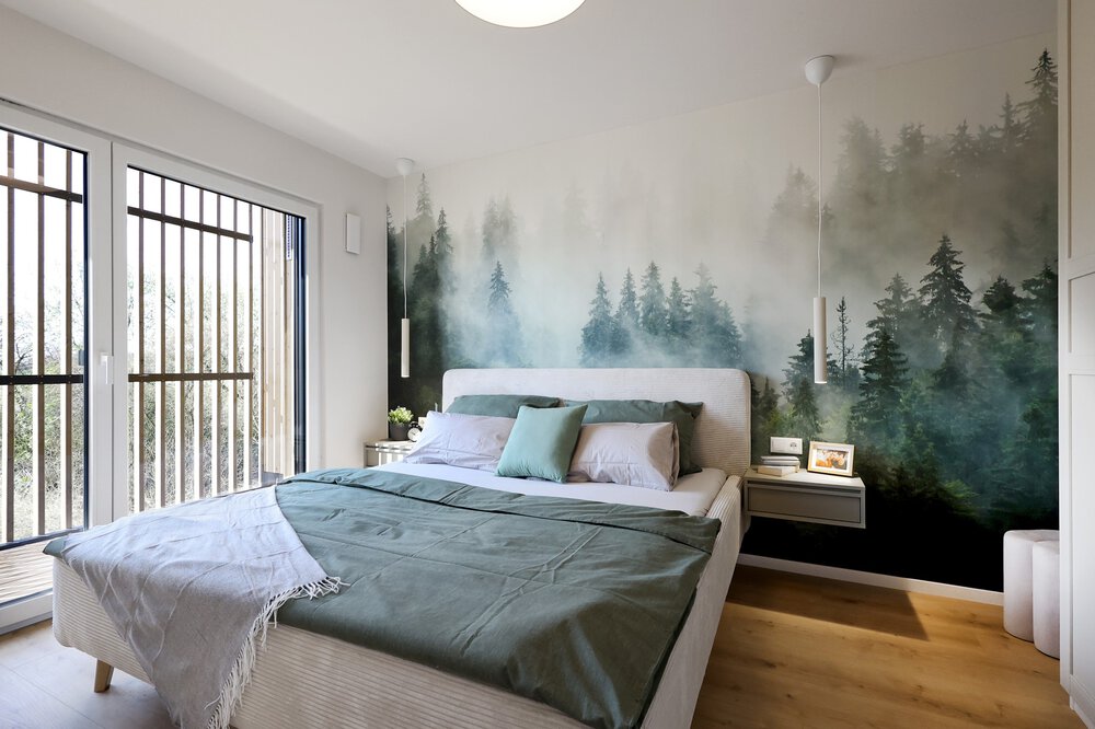 Großes Schlafzimmer mit Waldtapete, großen Fenstern, Doppelbett, grüner Bettwäsche und Holzboden.