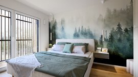 Großes Schlafzimmer mit Waldtapete, großen Fenstern, Doppelbett, grüner Bettwäsche und Holzboden.