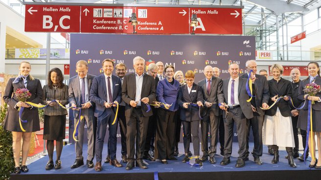 Eine Gruppe von Menschen in Business Kleidung steht bei einer feierlichen Eröffnung auf einer Bühne der BAU und zerschneiden ein buntes Band.