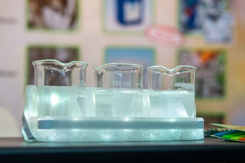 Three beakers filled with liquid on a table at a trade show