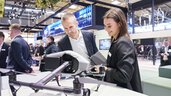 Two people look at a drone at the BAU 2025 trade fair. Other trade fair visitors can be seen in the background.