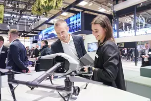 Two people look at a drone at the BAU 2025 trade fair. Other trade fair visitors can be seen in the background.