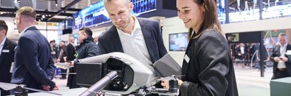 Auf der Messe BAU 2025 betrachten zwei Personen eine Drohne. Im Hintergrund sind weitere Messe-Besucher zu sehen.