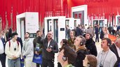 A group of trade fair visitors take part in a guided tour with headphones. In the background, exhibits can be seen between curtains of red strips hanging from the ceiling.