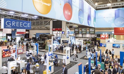 Vogelperspektive über den Innenraum einer gut besuchten Ausstellungshalle der transport logistic mit zahlreichen Plakaten, Ständen und Networking-Möglichkeiten.