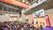 Interview auf der „Sportbühne“ der Messe f.re.e mit großem Publikum, einem Moderator und Sebastian Ströbl als Gast, während ein Bildschirm den Gast zeigt.