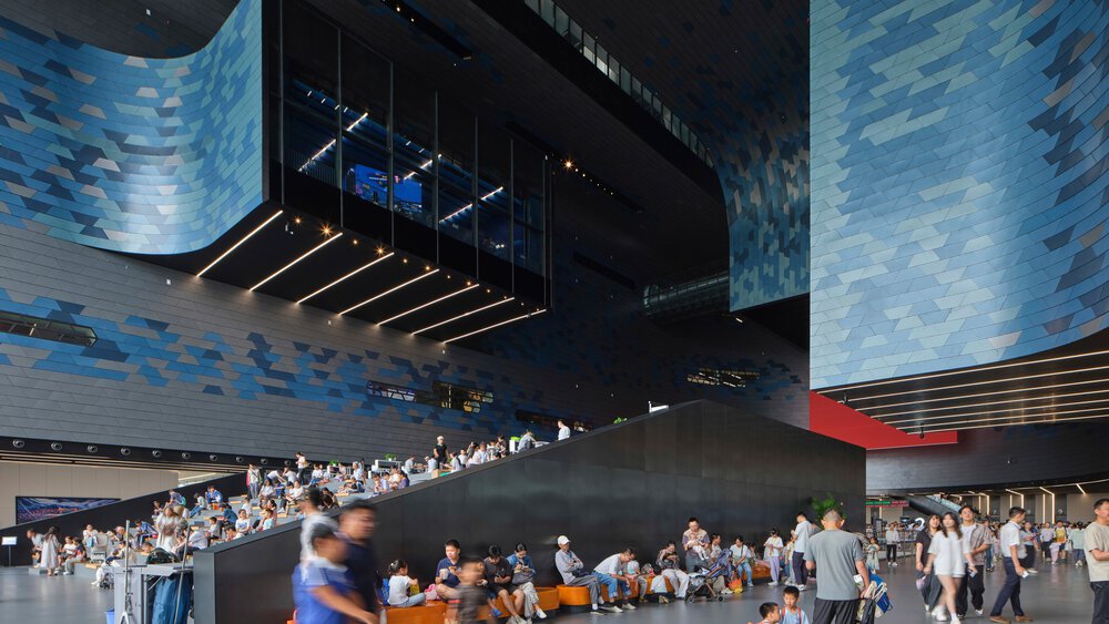 The interior of a hall-like futuristic building with large curved blue-grey walls and numerous visitors.