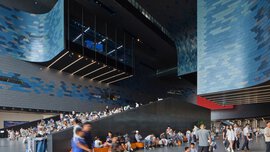 The interior of a hall-like futuristic building with large curved blue-grey walls and numerous visitors.