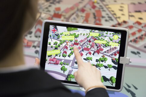 Person using a tablet on which a digital 3D map with buildings and trees is displayed.