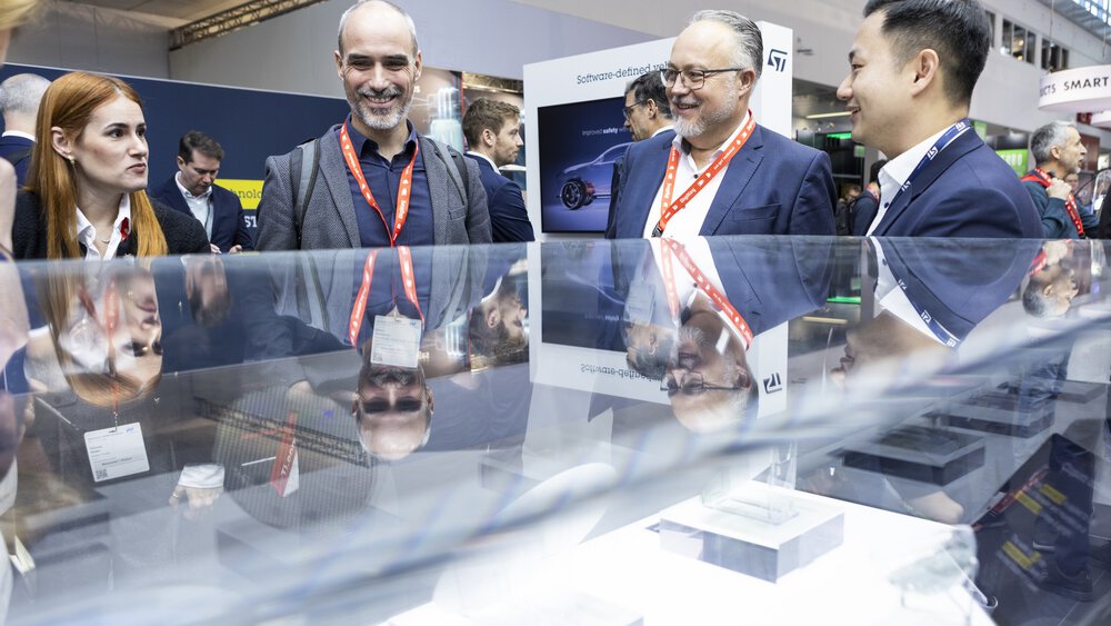 Four people in business attire are talking and smiling at a trade fair or conference stand.