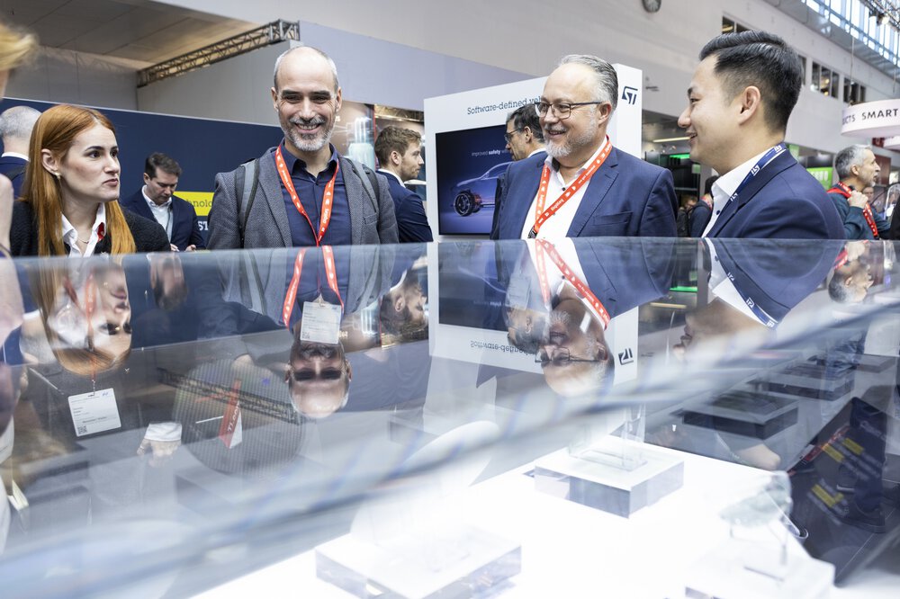 Vier Personen in Geschäftskleidung unterhalten sich und lächeln am Stand einer Messe oder Konferenz.