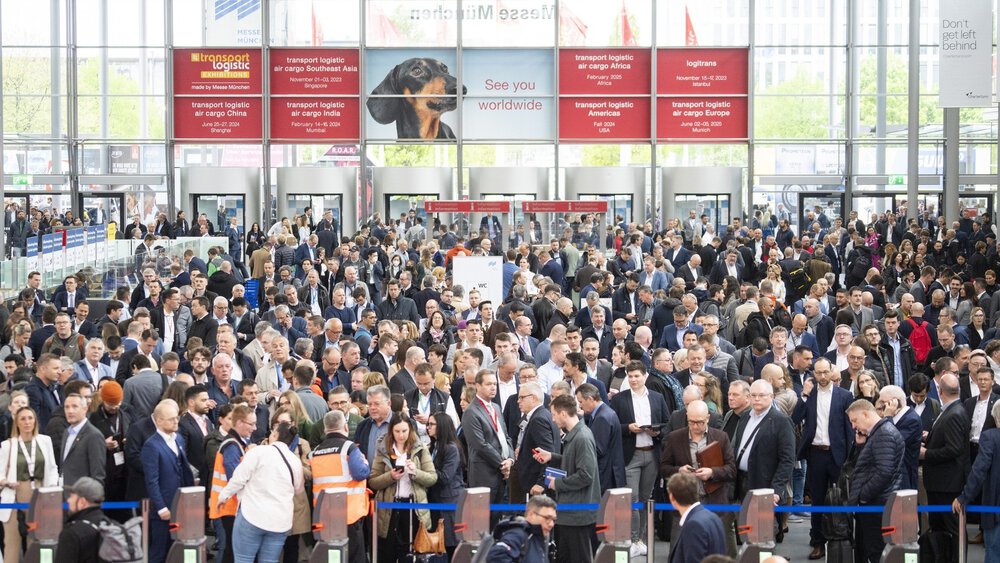 Zahlreiche Besucher warten auf den Einlass. Über den Eingängen hängen die Veranstaltungstermine der internationalen transport logistic-Messen.