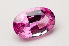 Close-up view of a pink gemstone with multiple, even cuts in an oval shape, resting on a white base.