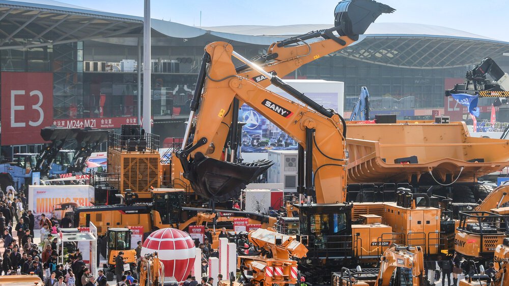 Large yellow construction vehicles and machines on display at a bustling outdoor trade show where people are walking around.