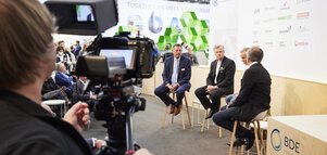 Sicht über die Schulter eines Kameramanns auf eine Podiumsdiskussion mit 4 Teilnehmern auf der Bühne der BDE in einer Messehalle.