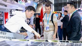 Ein Aussteller auf der BAU CHINA zeigt zwei Besuchern eine Vorrichtung für Solarpanele. Im Hintergrund sind weitere Messebesucher vor anderen Ständen zu sehen.
